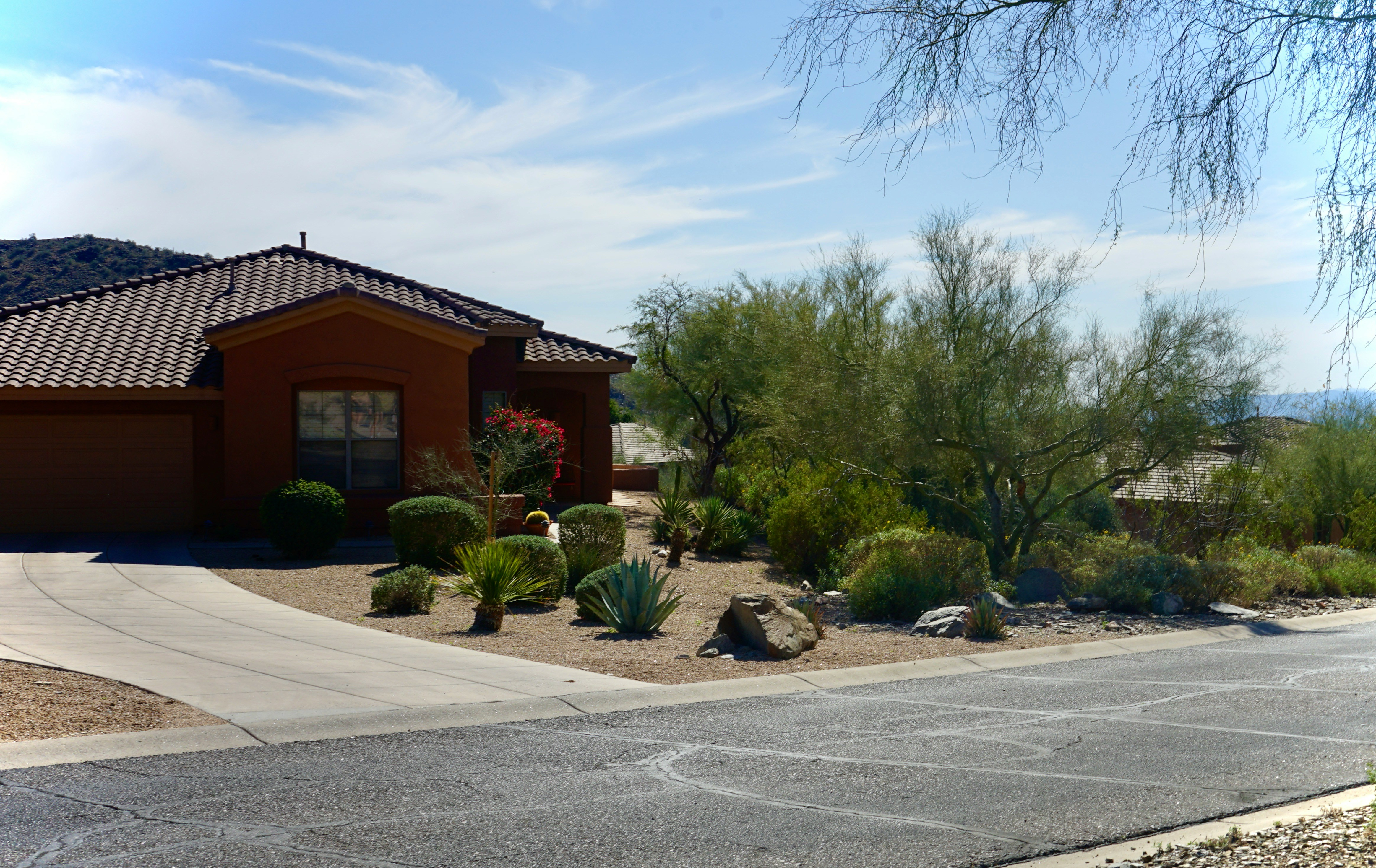 Desert home with xeriscape landscaping and a wide asphalt driveway prominent in the foreground